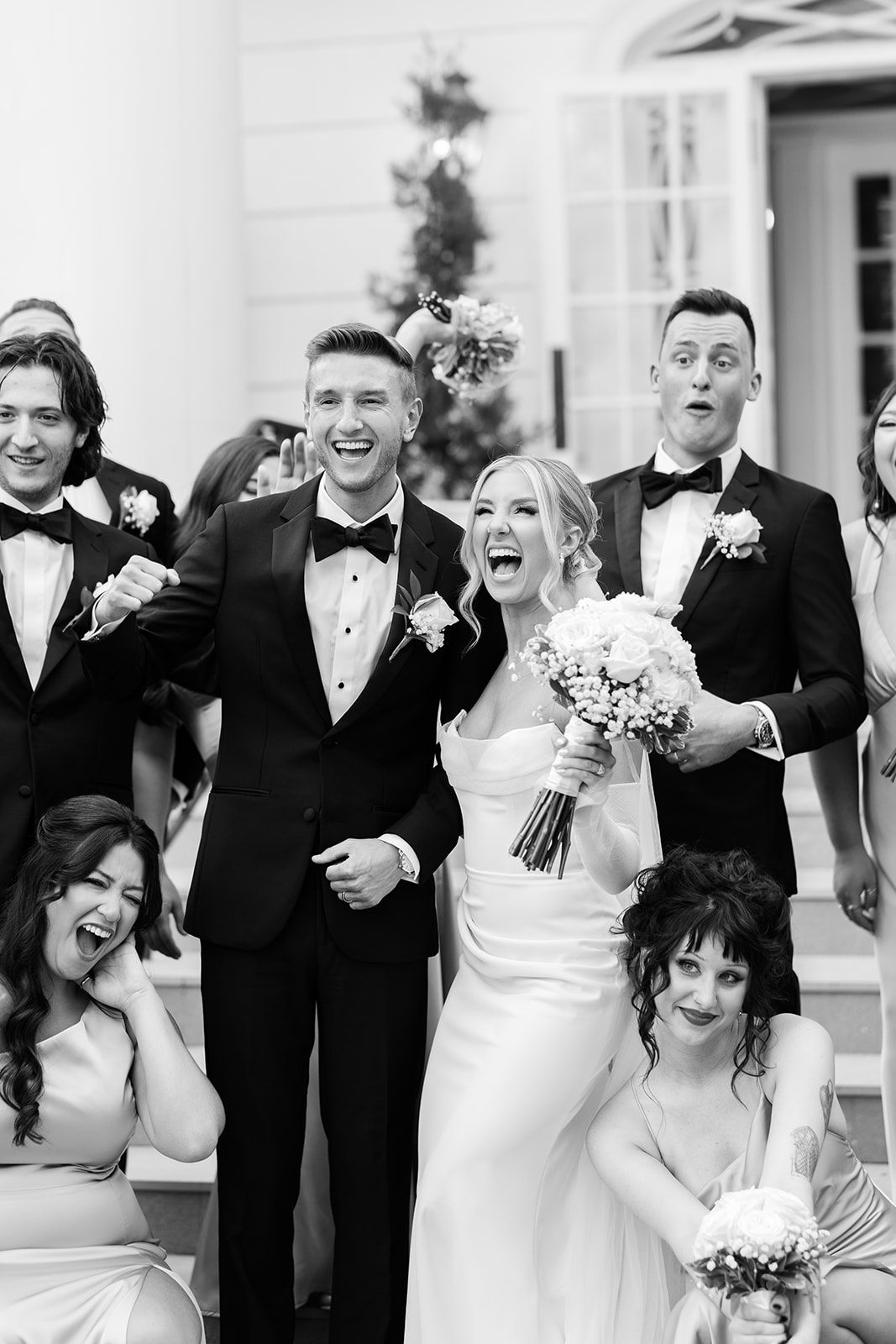 Black and white photo of the newlyweds laughing and cheering with their wedding party on the steps.